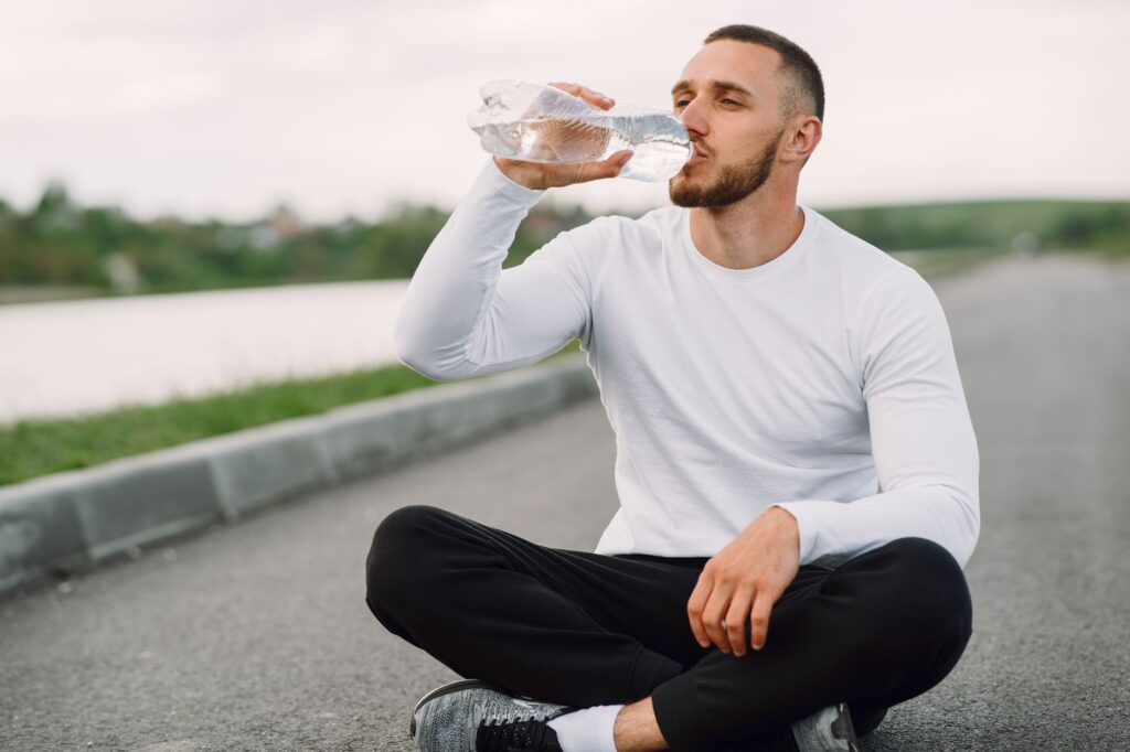 Man sitting outdoors drinking water after exercise — illustrating daily hydration and movement habits for gut health
