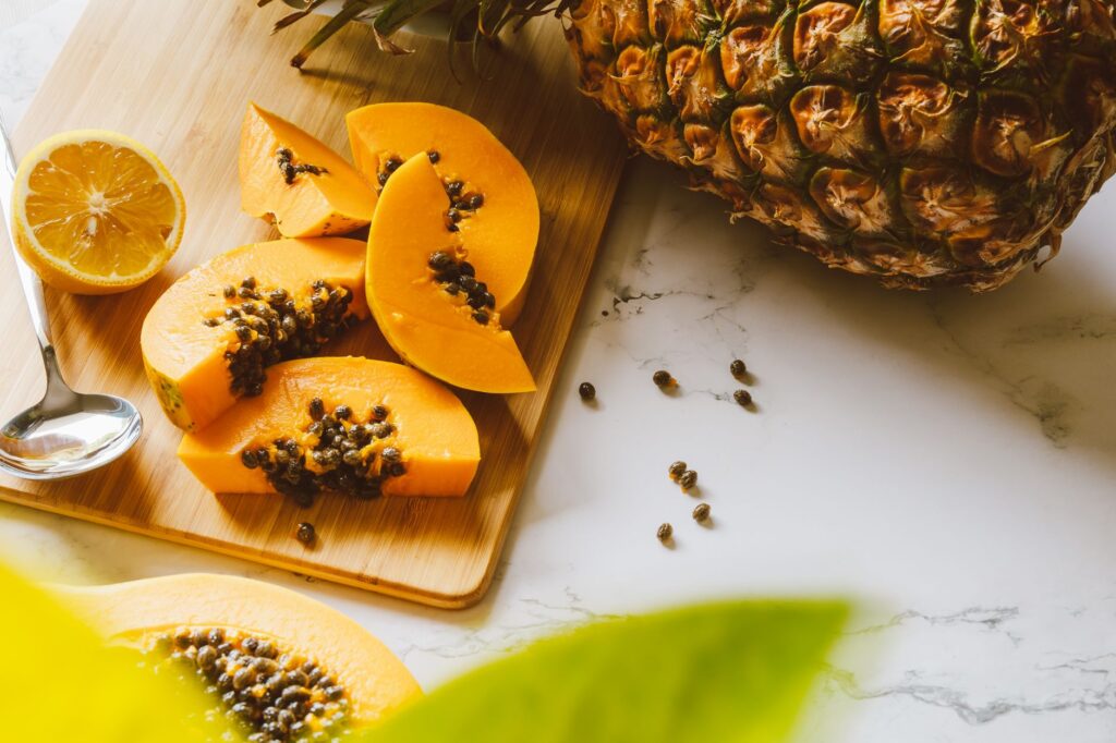Sliced papaya and lemon on a wooden cutting board with a whole pineapple, natural foods that support digestion