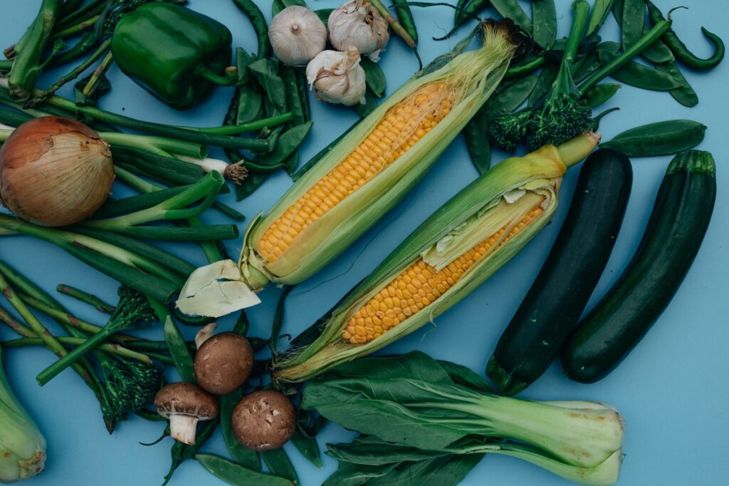Fresh prebiotic vegetables including garlic, onions, corn, broccoli, and cucumbers spread on a blue background