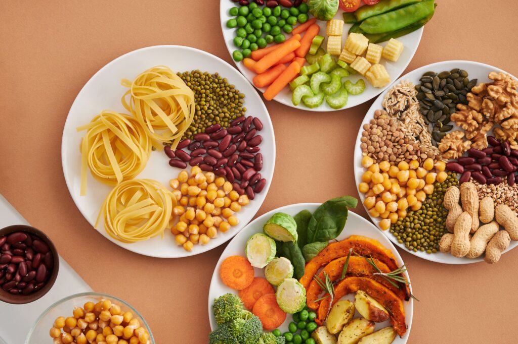 A spread of gut-friendly foods including legumes, chickpeas, nuts, vegetables, and whole grains arranged on white plates