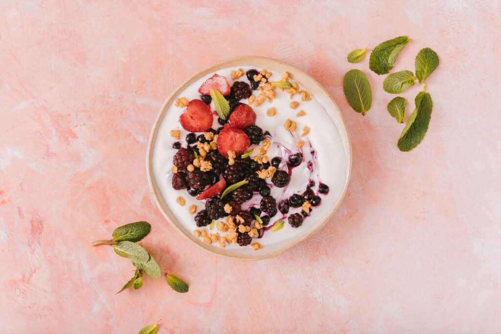 A yogurt bowl with live cultures topped with mixed berries, granola, and mint leaves — a probiotic-rich gut health food