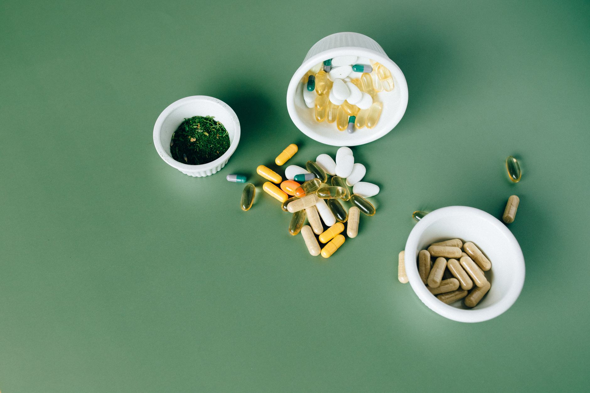 Various probiotic supplement capsules and pills in white bowls on a green background, representing the best probiotic supplements for gut health