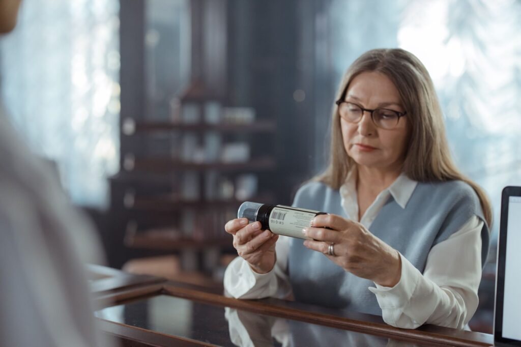 A senior woman wearing glasses carefully reads the label on a supplement bottle, representing the importance of checking probiotic supplement ingredients and strain details