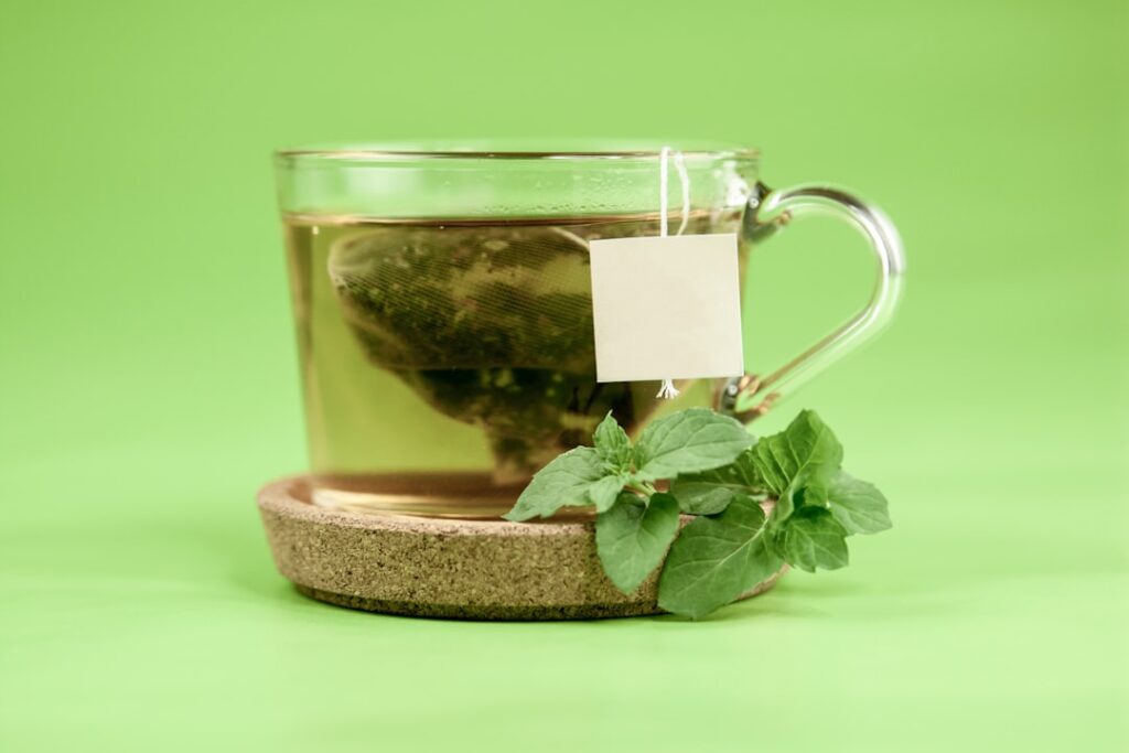 Glass mug of herbal peppermint tea with fresh mint leaves on a green background — natural digestive remedy