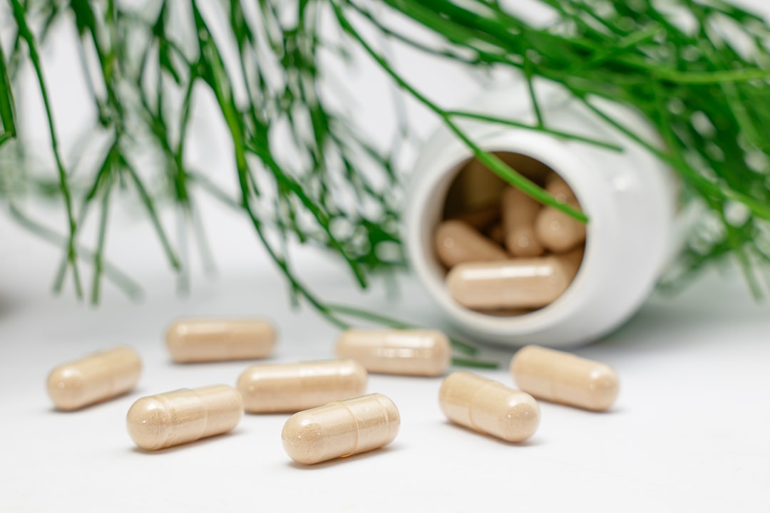 Gut health supplement capsules spilled from a white bottle next to green herbs, representing top gut health supplements for digestive support. Photo by Supliful on Unsplash.